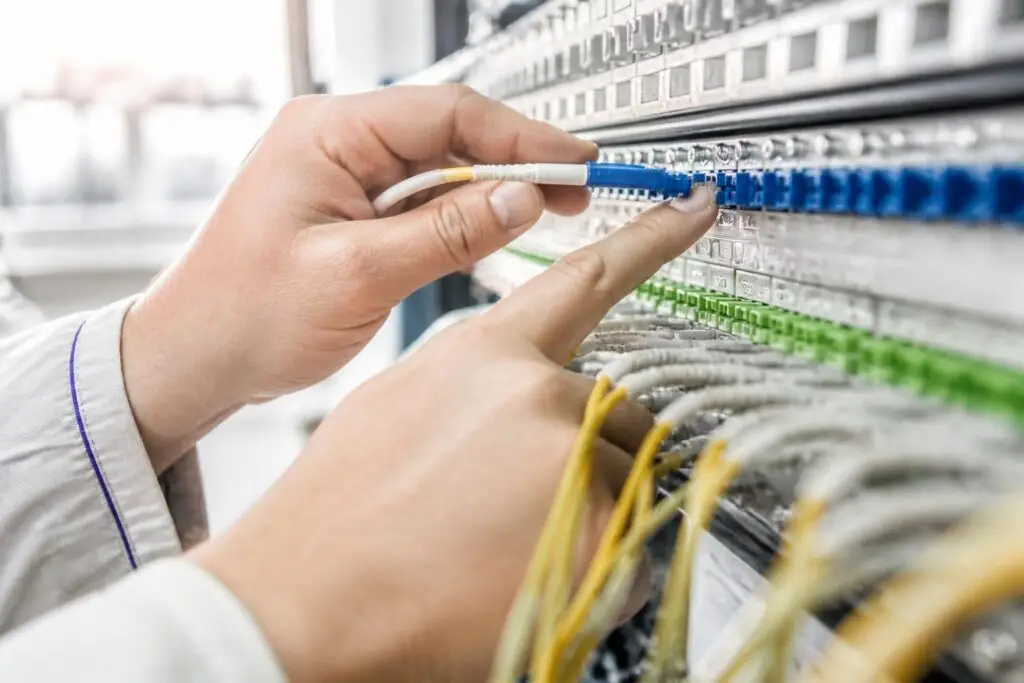 A hand is plugging a cable into a network panel.