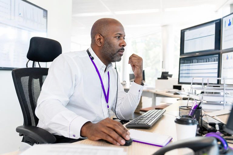 A man sits at a desk with multiple monitors displaying charts.