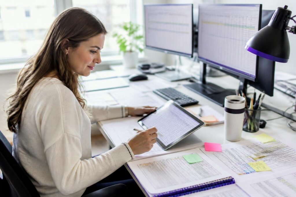 A woman working at a desk with multiple screens and a tablet.
