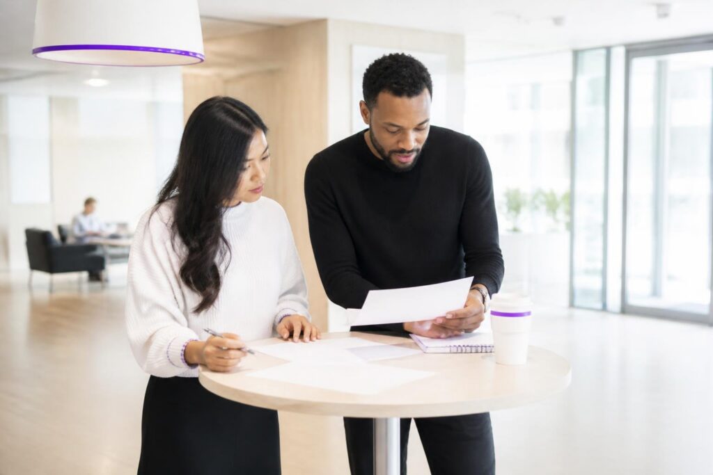 Two people stand at a table looking at documents.