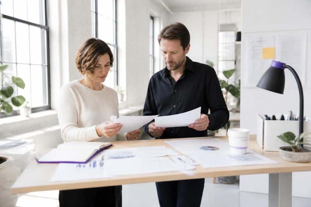 Two people stand at a table reviewing documents.