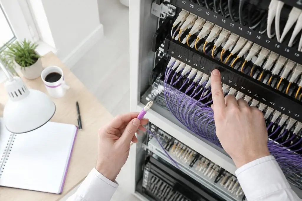 A person is working on a server rack with cables.