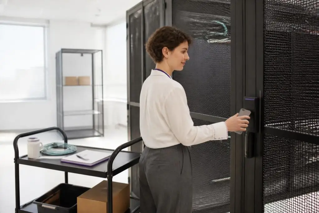 A person stands in front of a server room holding a smartphone to an access control system.