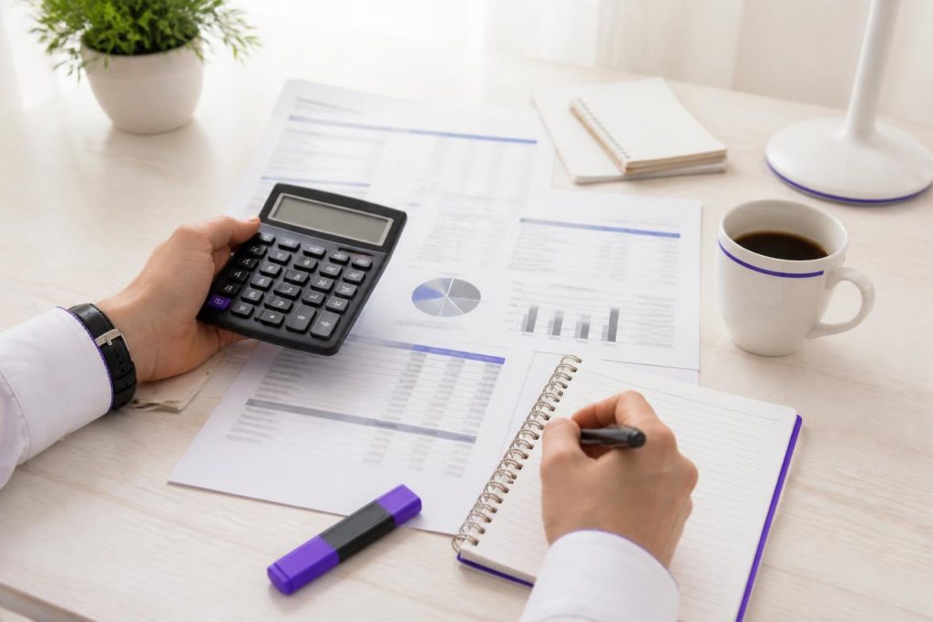 A person uses a calculator and takes notes on a desk with documents.