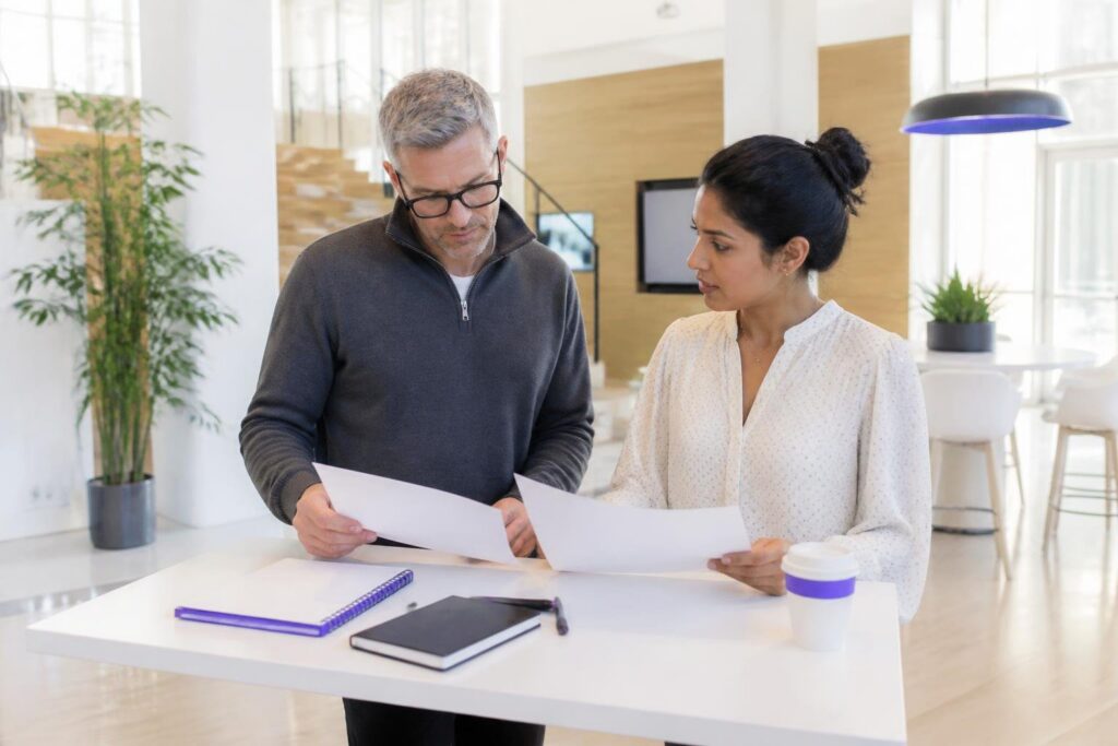 Two people looking at documents at a table in a modern office.