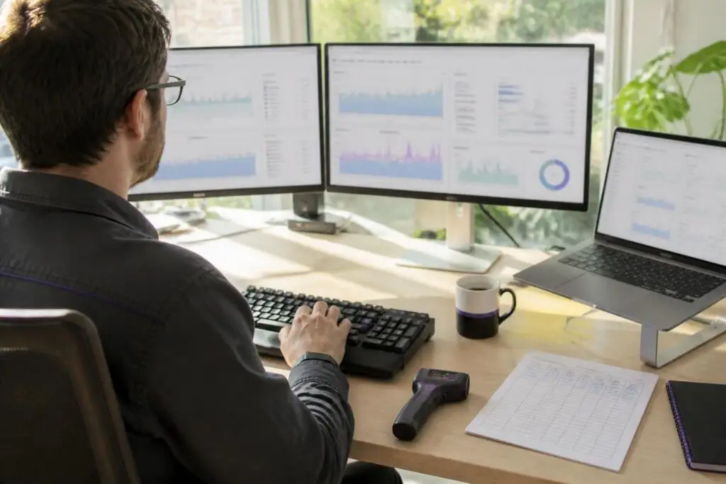 A man works at a desk with multiple monitors displaying charts.