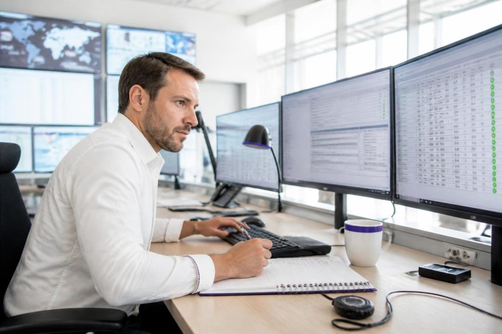 A man is working at multiple computer monitors in a modern office.