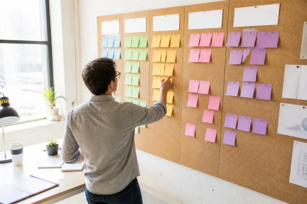 A person arranges colorful sticky notes on a corkboard.