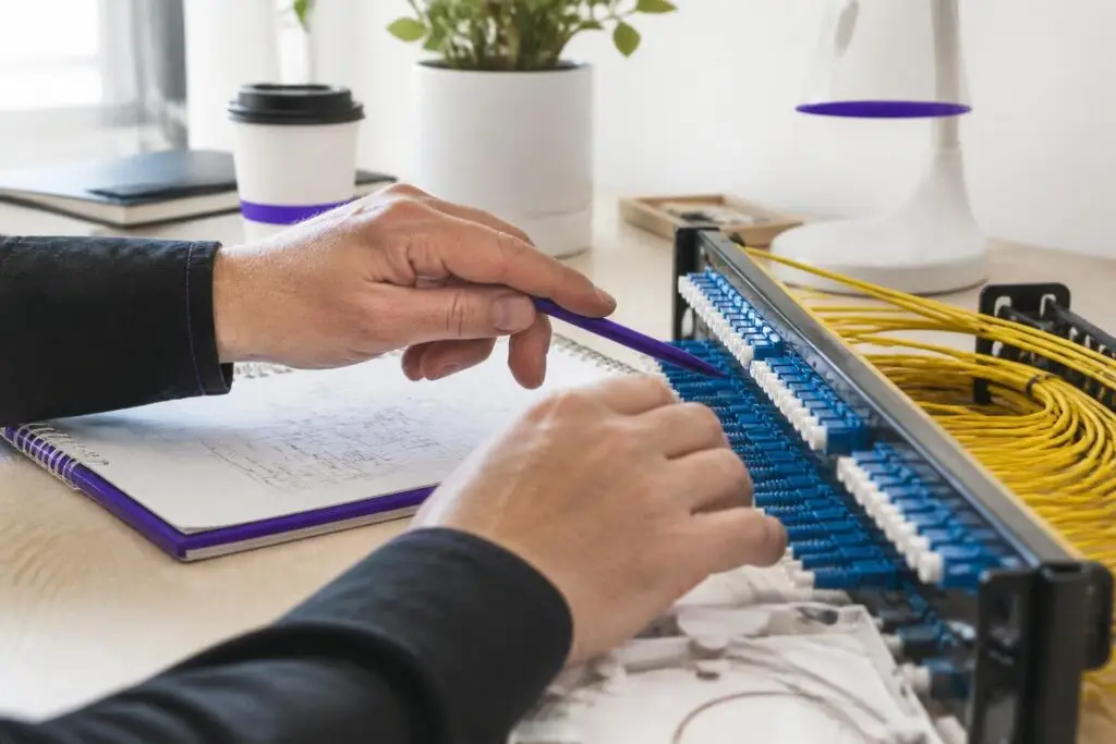 A person is working on a network patch panel with yellow cables.