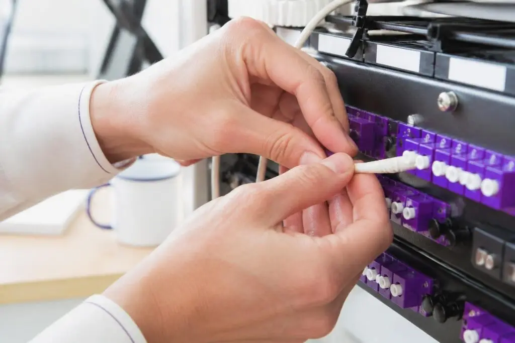 A person is plugging a cable into a server rack.