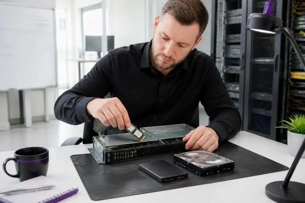 A man installs an NVMe drive into a server case, with an SSD and an HDD next to it.