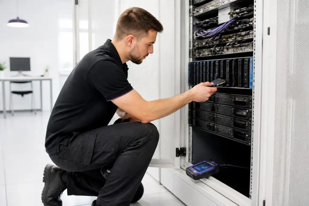 A technician is working on a server rack in a bright room.