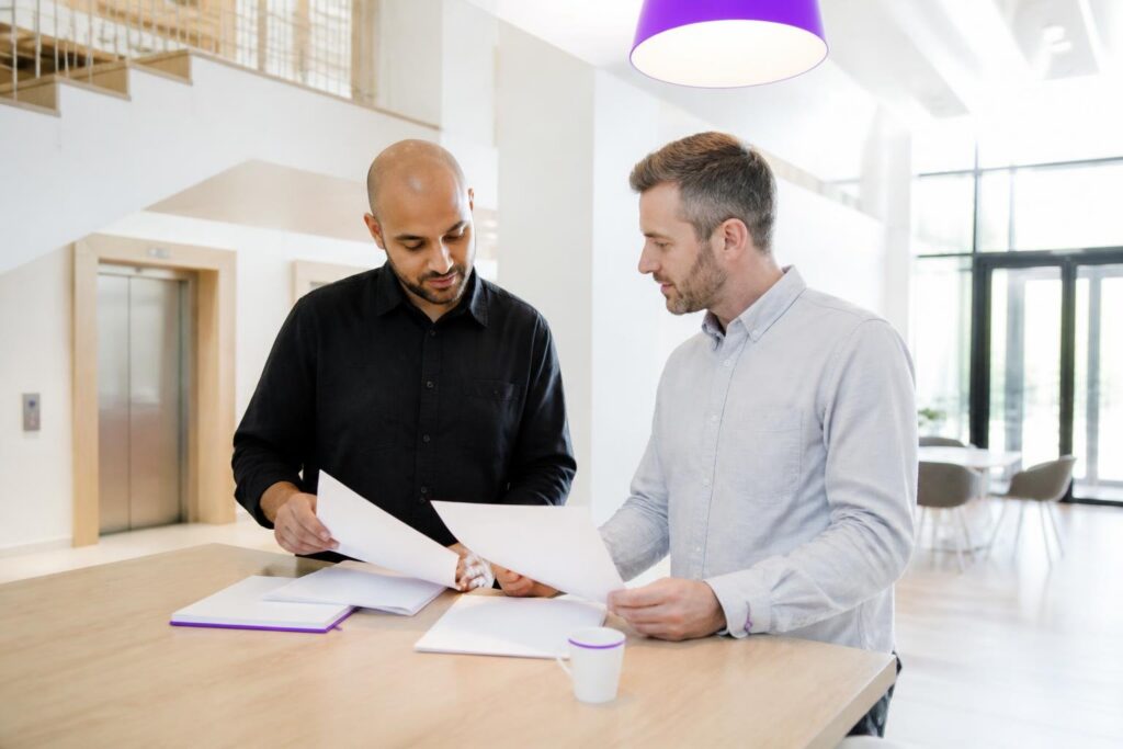 Two men standing at a table reviewing documents in a modern office.