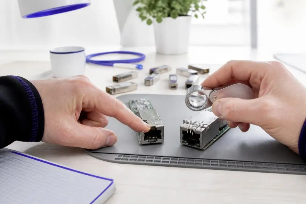 Two hands examining network components with a magnifying glass.