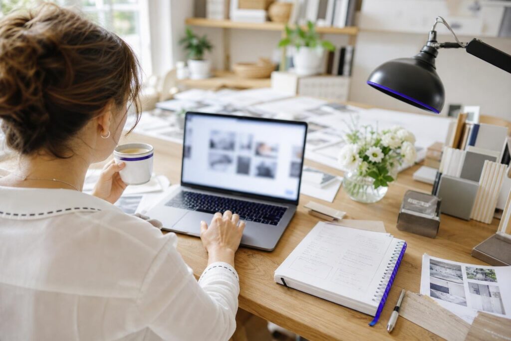 A person working on a laptop at a desk with a notebook and flowers.