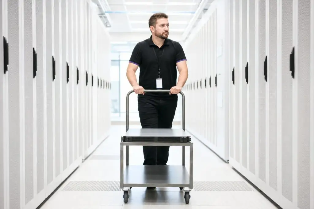 A man pushes a cart through a server room.